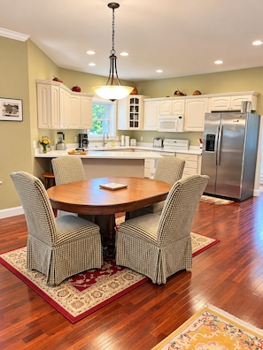 A kitchen with white cabinets, a stainless steel refrigerator, and a dining table with checkered chairs. - South Main Street Cottage - Leland, Michigan - Saturday to Saturday (Leland)
