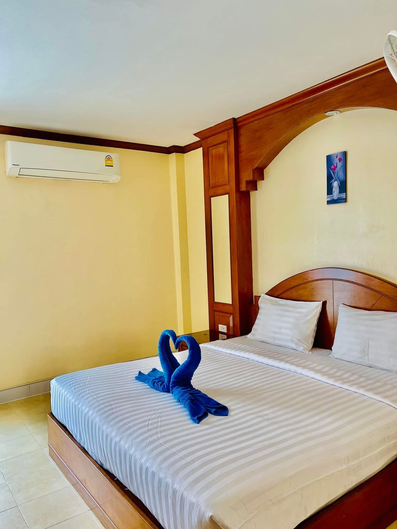A hotel room with a bed, a wall-mounted air conditioner, and a painting on the wall.