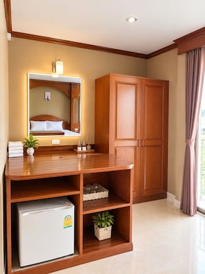 A hotel room with a wooden desk, a refrigerator, a mirror, and a wardrobe. - Innarm House Patong  (Kathu District, Phuket, Thailand.)