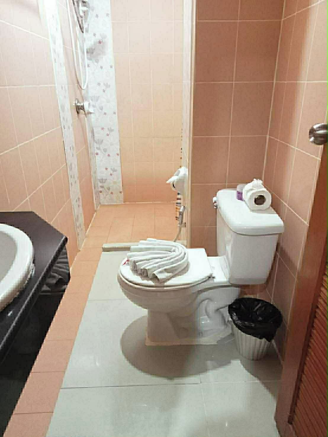 A small bathroom with a toilet, a shower, and a trash bin.