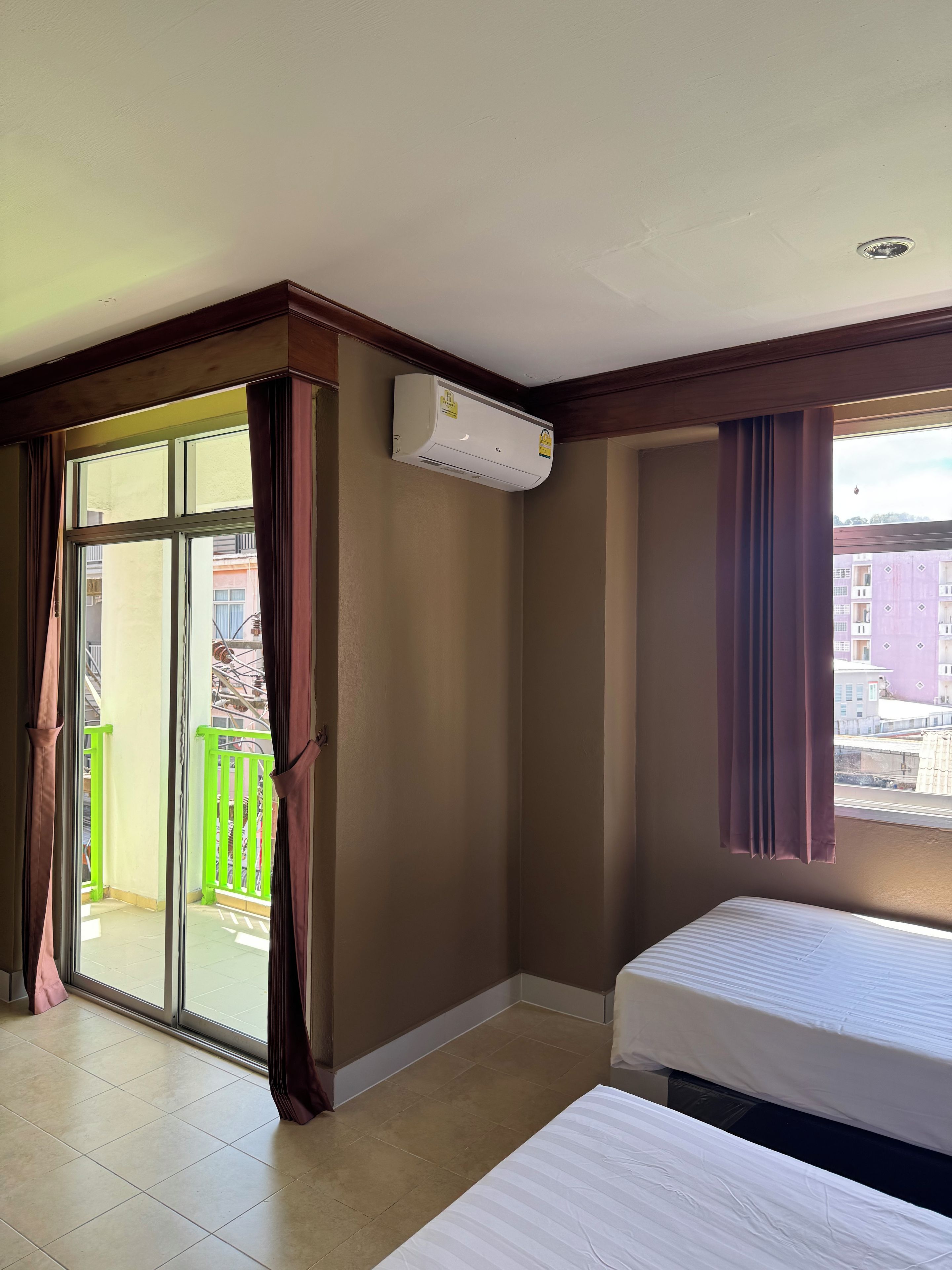 Quarto de hotel com cama, porta de vidro deslizante para uma varanda externa e ar condicionado instalado no teto.