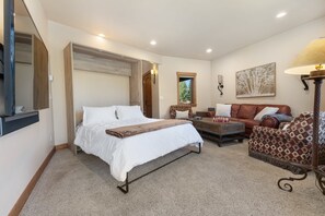 Een slaapkamer met een bed, een slaapbank, een bijzettafeltje en een lamp.