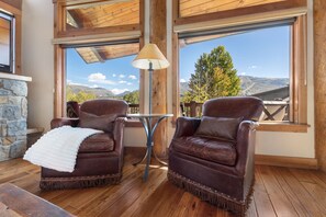 A cozy seating area with two leather chairs, a table, and a lamp, overlooking a scenic mountain view. - Trollhaugen Lodge | 4BR, Sleeps 10, Near Ski Base (Steamboat Springs)