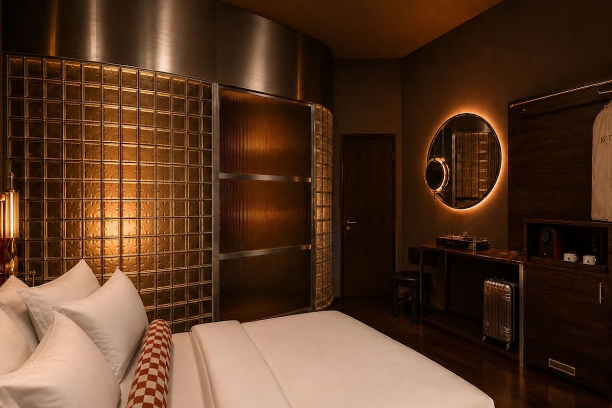 A modern hotel room with a large bed, a wardrobe, a mirror, and a small seating area.