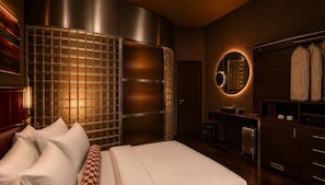 A modern hotel room with a large bed, a wardrobe, a mirror, and a small seating area. - Koti (Cape Town)