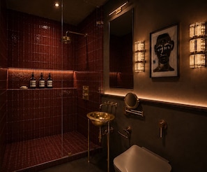 A bathroom with a glass-enclosed shower, a gold sink, and a large mirror. - Koti (Cape Town)