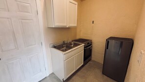A compact kitchen with white cabinets, a double sink, a stove, and a black refrigerator. - 2-bedroom apartment cheaper than a hotel, beats the size and price of a hotel. (Presidio)