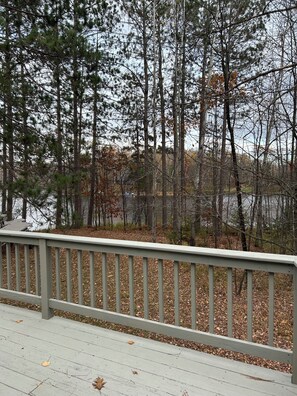 A wooden deck with a railing overlooking a forested area with trees and a body of water. - Cozy Cabin on a Private Point — Water Views on 3 Sides, Fishing & Trail Access (Irma)