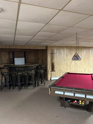 A pool table with a red felt surface, surrounded by black chairs. - Cozy Cabin on a Private Point — Water Views on 3 Sides, Fishing & Trail Access (Irma)