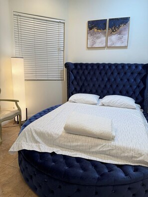 Ein Schlafzimmer mit einer gebügelten Kopfteil, einem Bett mit weißer Bettwäsche, einem Sessel, einer Nachttischlampe und zwei Wandbildern.