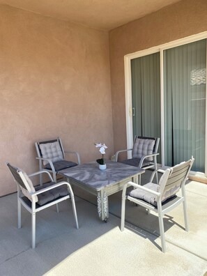 Un patio con una mesa, cuatro sillas, una planta en maceta y un ventanal corredero.