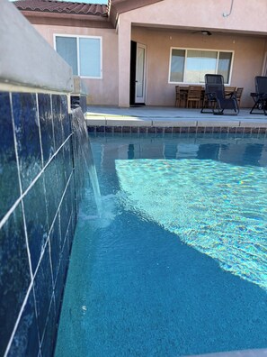 A swimming pool with a tiled edge, a patio area with outdoor furniture, and a building in the background. - Spacious 4-bedroom house in marvelous Desert Hot Springs with AC (Desert Hot Springs)