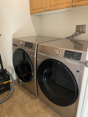 A compact laundry area with two front-loading washing machines and a vacuum cleaner. - Spacious 4-bedroom house in marvelous Desert Hot Springs with AC (Desert Hot Springs)
