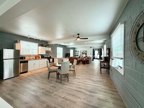A modern kitchen with a dining area, wooden flooring, and a large wall clock. - Luxurious 1 Bedroom 2nd Story Walk-Up (Wellsville)