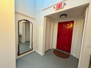A hallway with a red door, an exit sign, a mirror, and a doormat. - Luxurious 1 Bedroom 2nd Story Walk-Up (Wellsville)