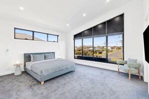 A modern bedroom with a large bed, a nightstand, a chair, and a view of the outside. - Indented Head Coastal Retreat | 5BR Escape (Indented Head)