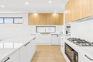 A modern kitchen with white cabinetry, a wooden accent wall, and a gas stove. - Indented Head Coastal Retreat | 5BR Escape (Indented Head)