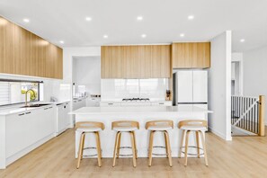 A modern kitchen with white cabinetry, a central island with bar stools, and a wooden ceiling. - Beachfront Retreat | 5BR 5Bath Sleeping 12 (Indented Head)