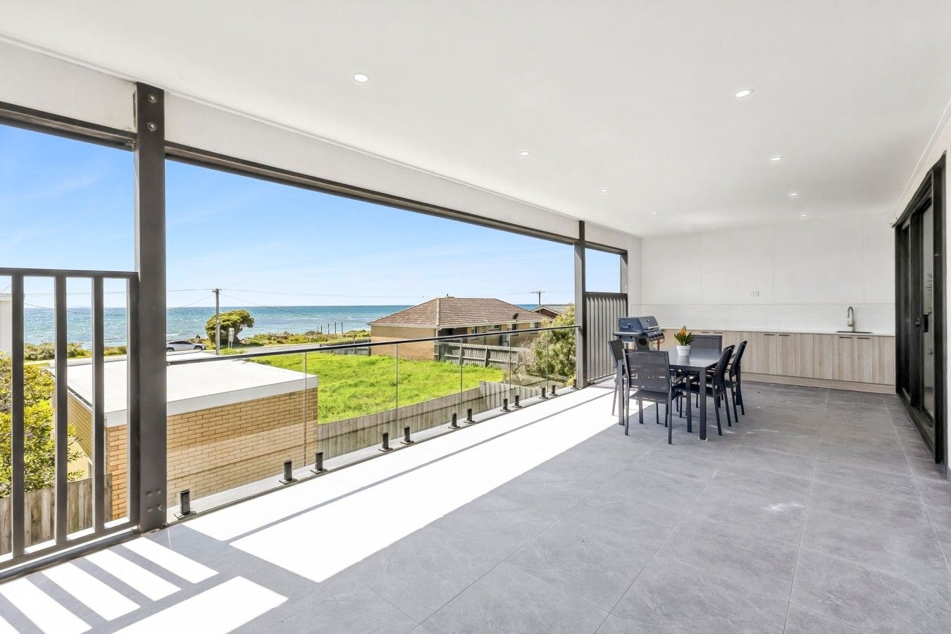 A balcony with a view of the sea, a barbecue grill, and a dining area with chairs and a table.