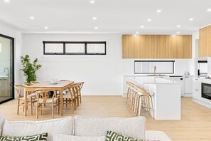 Une cuisine moderne avec des meubles blancs, un îlot central doté de tabourets de bar et un coin repas avec une table et des chaises en bois.