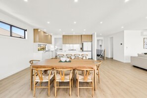 Une cuisine moderne avec des meubles blancs, un coin repas avec une table et des chaises en bois, et un salon avec un canapé.