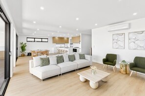 A modern living room with a sofa, two green armchairs, a coffee table, and a dining area with a table and chairs. - Beachfront Retreat | 5BR 5Bath Sleeping 12 (Indented Head)