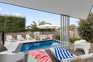 Ein Garten mit Swimmingpool, Liegestühlen, einer Sitzecke und einem Sonnenschirm.