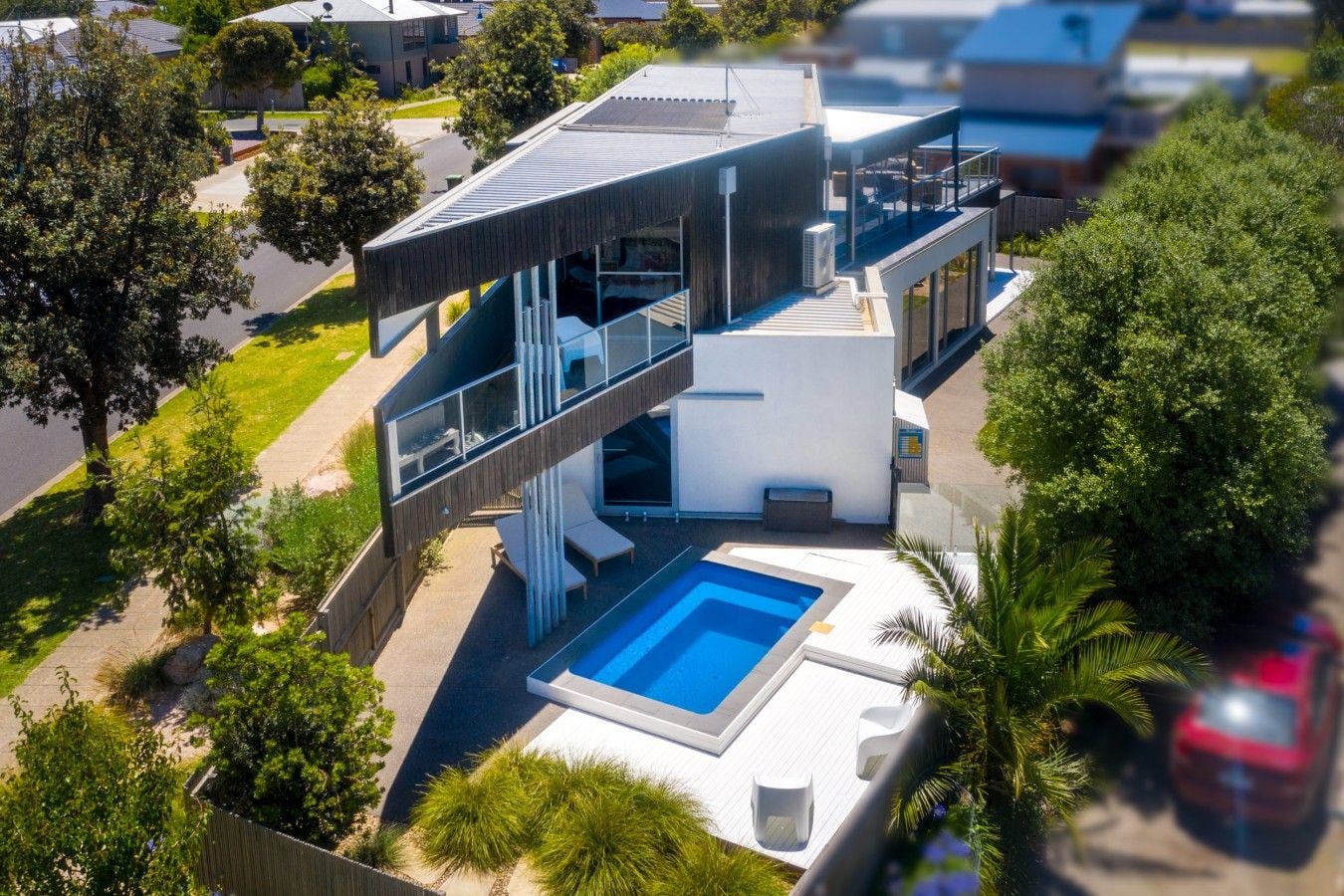 Een modern huis met twee verdiepingen, een zwembad, buitenmeubels en een overdekt terras.