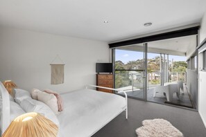 Ein modernes Schlafzimmer mit einem Bett, einem Fernseher, einem Balkon mit einem Sessel und Blick ins Freie.