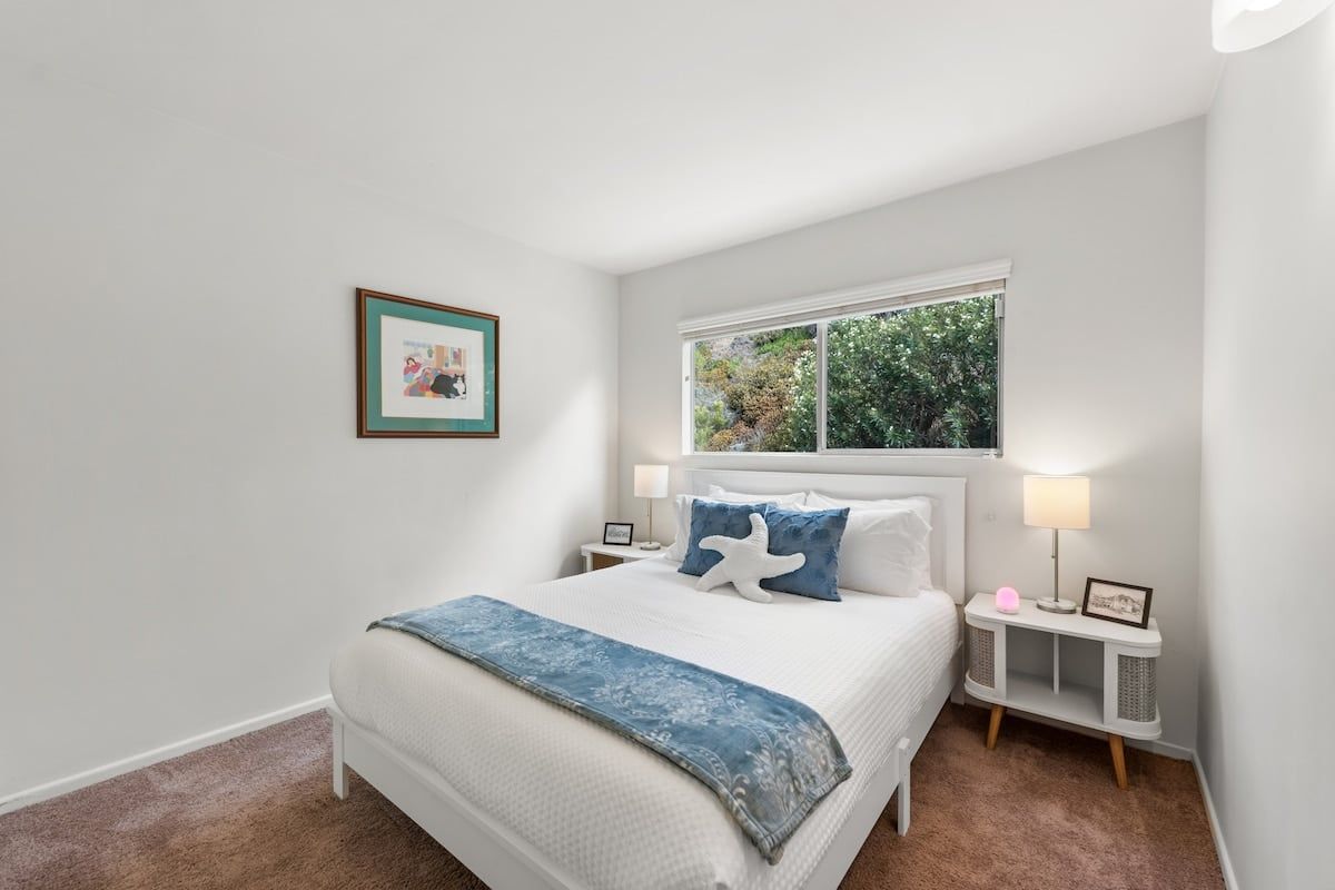 A bedroom with a bed, bedside tables, a window, and a framed picture on the wall.