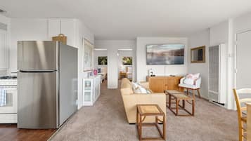 A modern kitchen with a stainless steel refrigerator, a dining area with a wooden table and chairs, and a living room with a beige sofa.