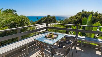 A balcony with a glass table and chairs, overlooking a scenic ocean view.