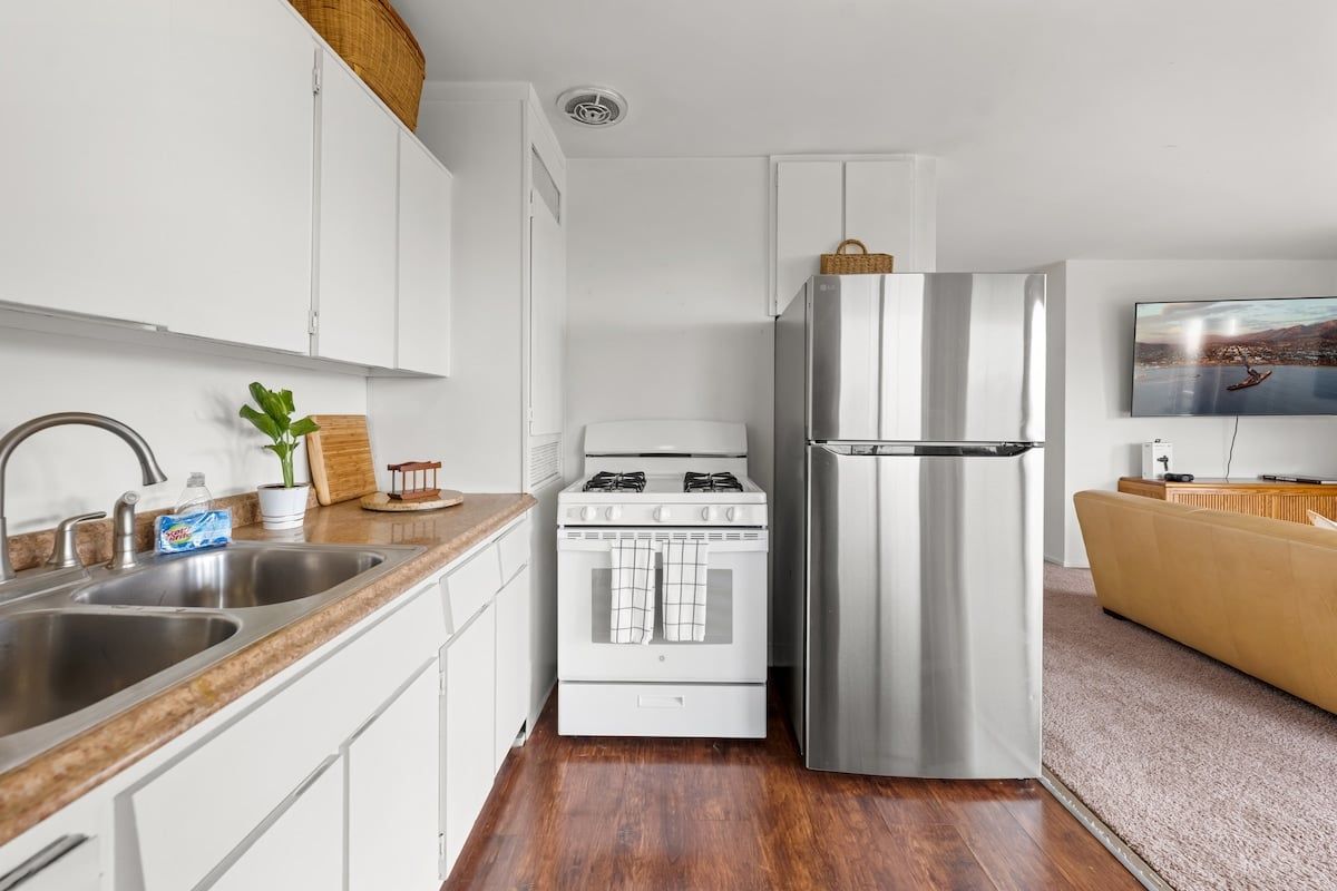 A modern kitchen with stainless steel appliances, a wooden countertop, and a flat-screen TV mounted on the wall.