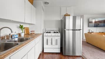 A modern kitchen with stainless steel appliances, a wooden countertop, and a flat-screen TV mounted on the wall.