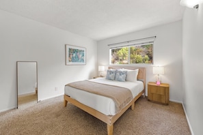 Un dormitorio con cama, ventana, mesita de noche y espejo.