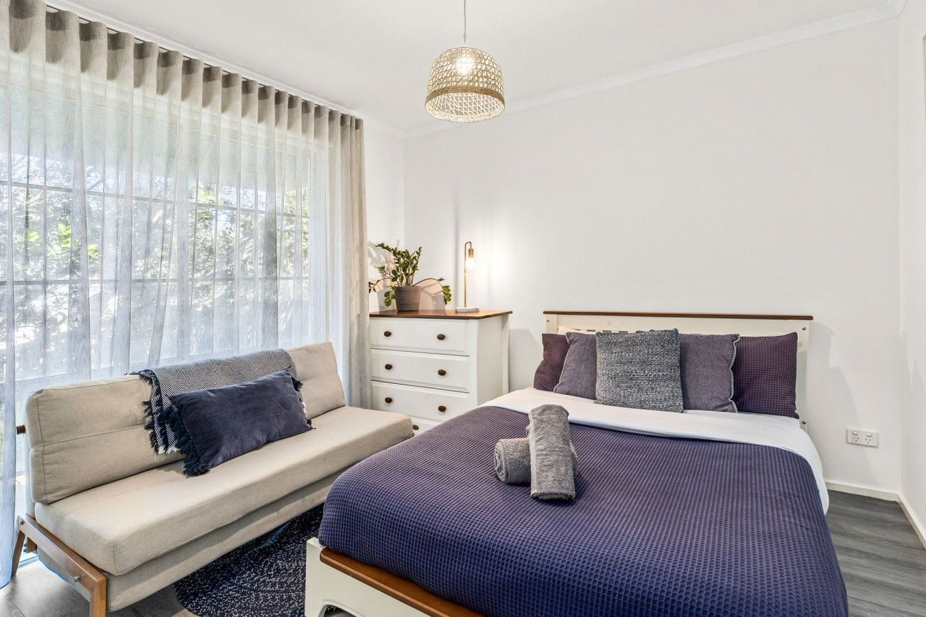 A bedroom with a bed, a sofa, a dresser, and a window with curtains.