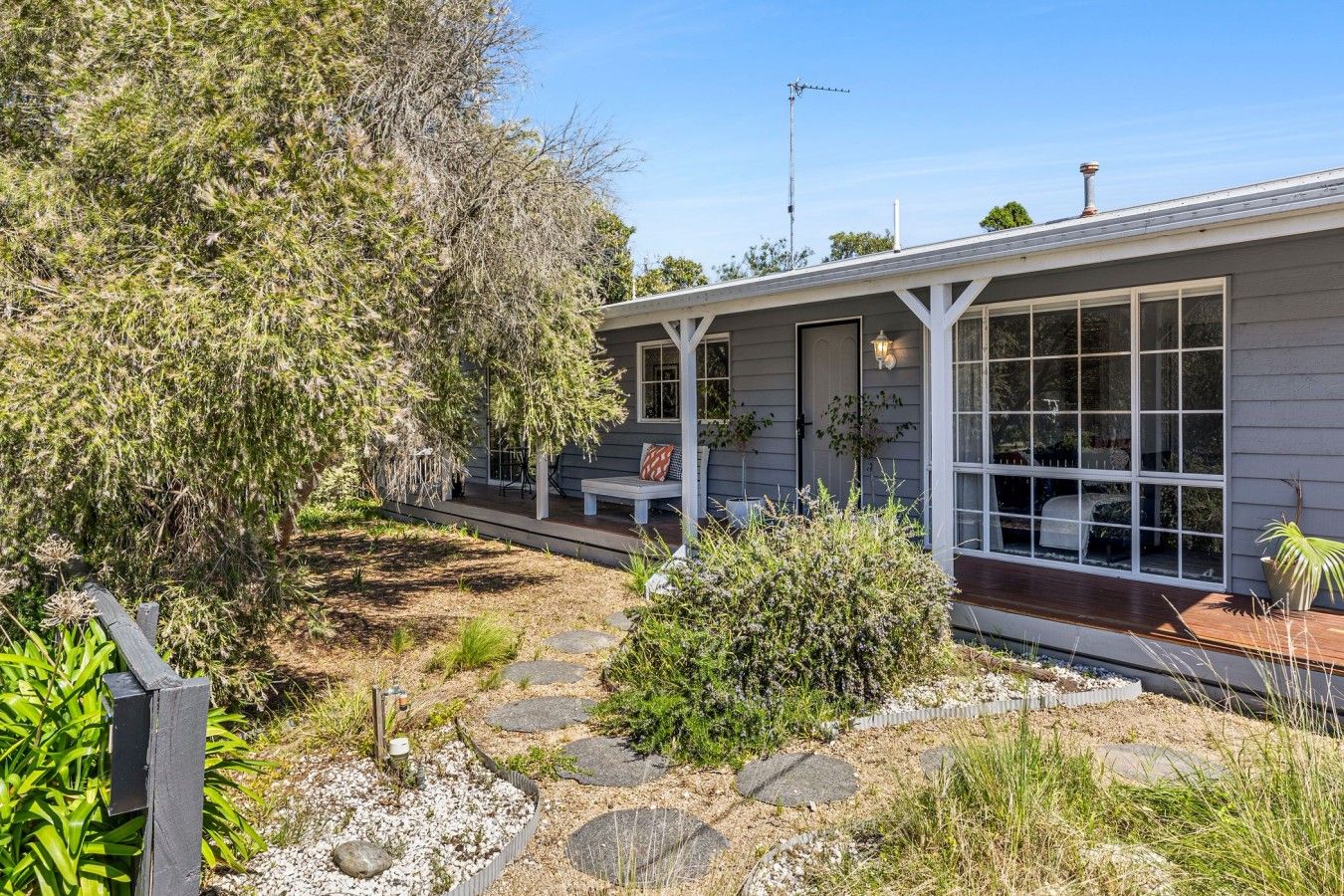 A house with a porch, a bench, and a garden with rocks and plants.