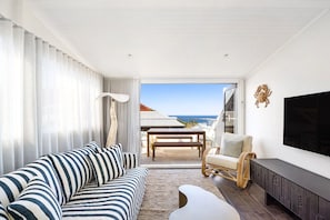 Ein modernes Wohnzimmer mit einer Couch, einem Fernseher und Blick aufs Meer.