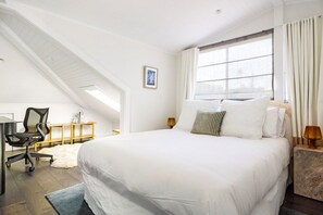 Ein Schlafzimmer mit einem großen Bett, einem Schreibtisch, einem Sessel und einem Fenster mit Vorhängen.