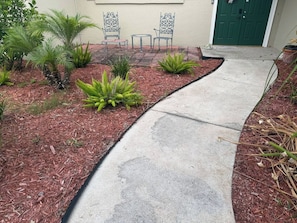 A concrete pathway leading to a door, surrounded by mulch and various plants. - Family Tiki Bar, Hot Tub & Grill • 5 min SRQ (Sarasota)