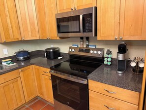 A kitchen with wooden cabinets, a microwave, a stove, a coffee maker, and a spice rack. - Family Tiki Bar, Hot Tub & Grill • 5 min SRQ (Sarasota)