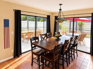 A dining area with a wooden table and chairs, a hanging light fixture, and an American flag on the wall. - Family Tiki Bar, Hot Tub & Grill • 5 min SRQ (Sarasota)