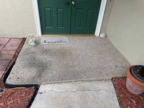 A concrete entryway with a doormat, a green door, and a potted plant. - Family Tiki Bar, Hot Tub & Grill • 5 min SRQ (Sarasota)