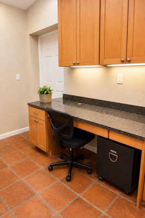A kitchen with wooden cabinets, a black office chair, a small potted plant, and a black storage unit. - Family Tiki Bar, Hot Tub & Grill • 5 min SRQ (Sarasota)