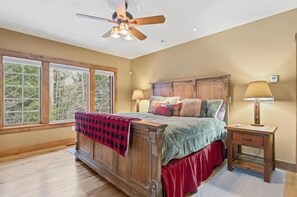 A bedroom with a wooden bed, two bedside tables, a ceiling fan, and large windows. - Ski Trail to Door | Hot Tub, Games & Gym (Lincoln)