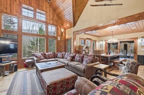 A spacious living room with a large television, comfortable seating, and a dining area with a chandelier. - Ski Trail to Door | Hot Tub, Games & Gym (Lincoln)