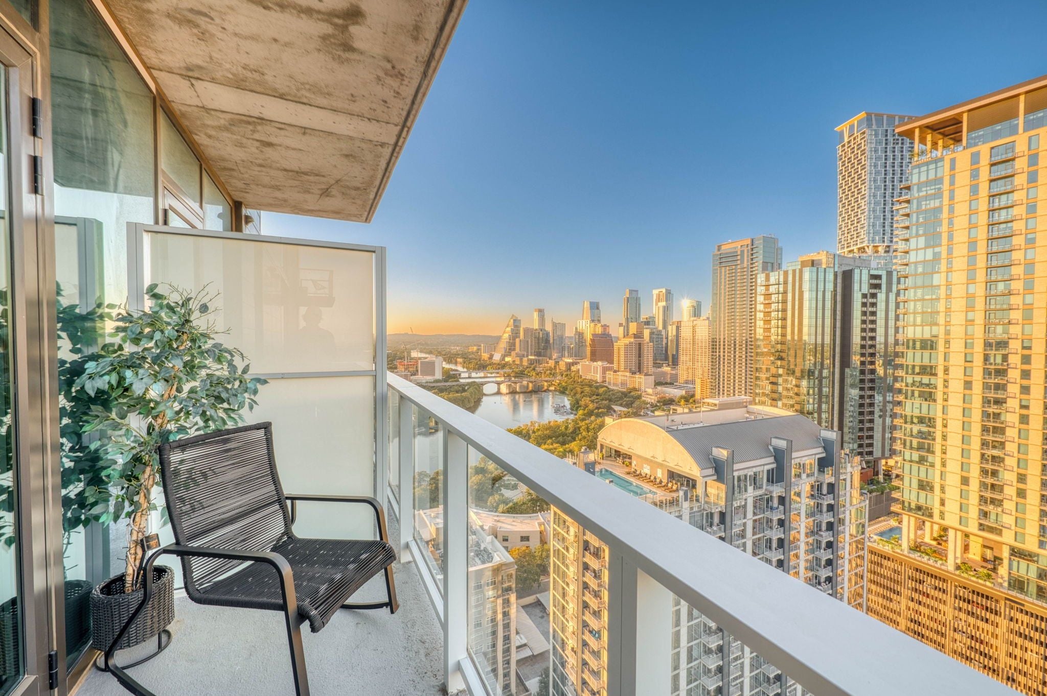 A balcony with a view of a city skyline, a chair, and a potted plant.