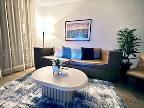 A living room with a sofa, a coffee table, a framed picture on the wall, and a potted plant. - 🌅 Rainey Street Retreat | Lake Views, Rooftop Pool & 31st Floor Skyline 🎸 (Austin)