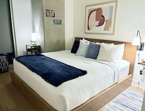 A hotel room with a bed, a nightstand, a lamp, a sign indicating the location, and a wall art piece. - 🌅 Rainey Street Retreat | Lake Views, Rooftop Pool & 31st Floor Skyline 🎸 (Austin)