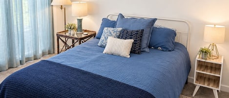 A bedroom with a bed, two bedside tables, a lamp, a rug, and a window with curtains.